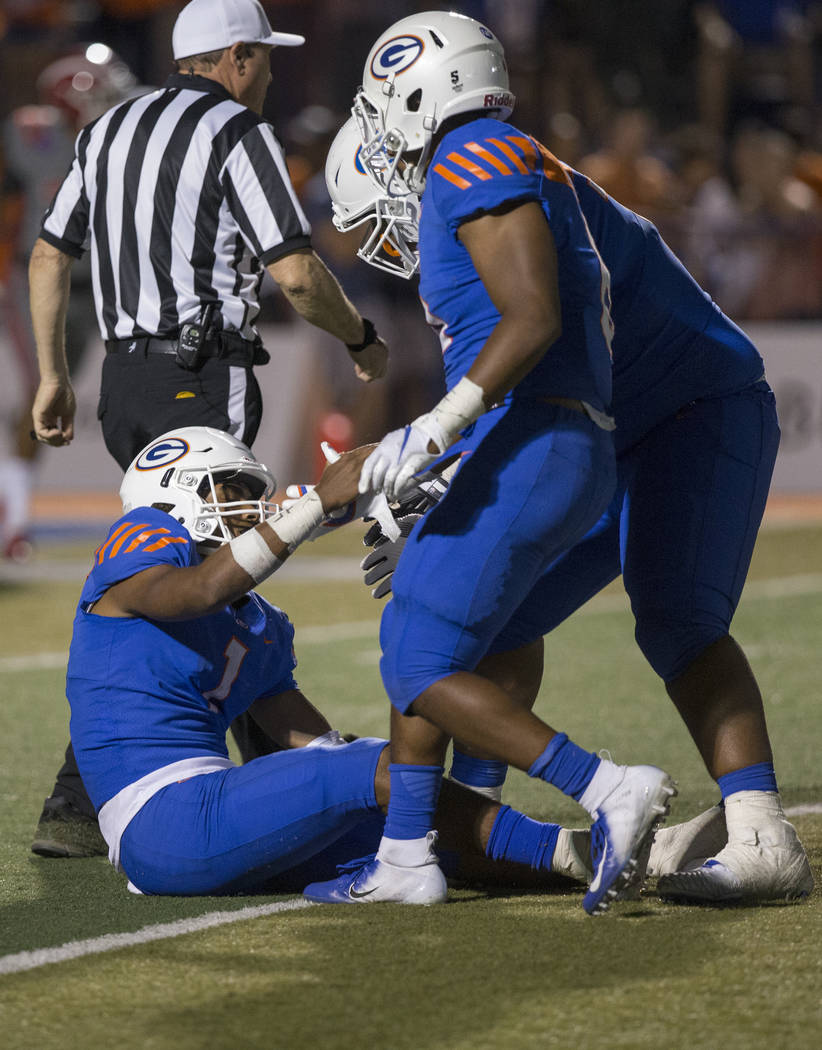 Bishop Gorman junior quarterback Micah Bowens (1) is helped up by teammates after taking a big hit in the third quarter during the Gaels home matchup with Mater Dei on Friday, Aug. 24, 2018, at Bi ...