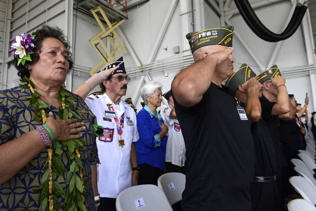 Audience members stand during the National Anthem at a ceremony marking the arrival of the remains believed to be of American service members who fell in the Korean War at Joint Base Pearl Harbor- ...