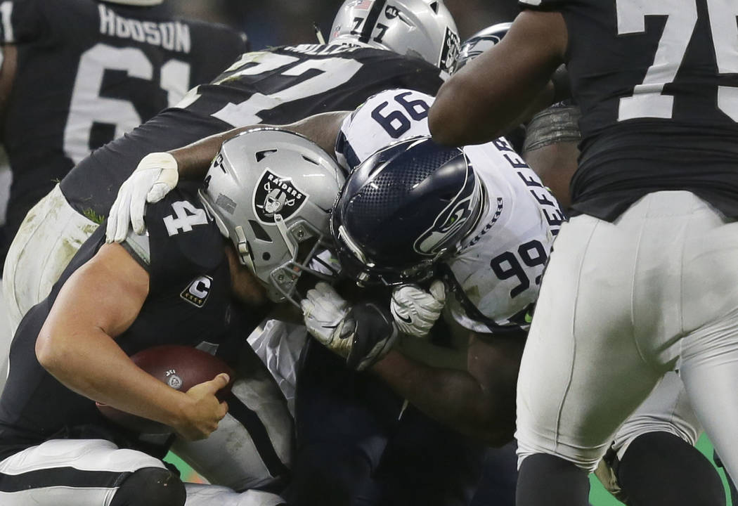 Oakland Raiders quarterback Derek Carr (4) is grabbed by Seattle Seahawks defensive tackle Quinton Jefferson (99) during the first half of an NFL football game at Wembley stadium in London, Sunday ...