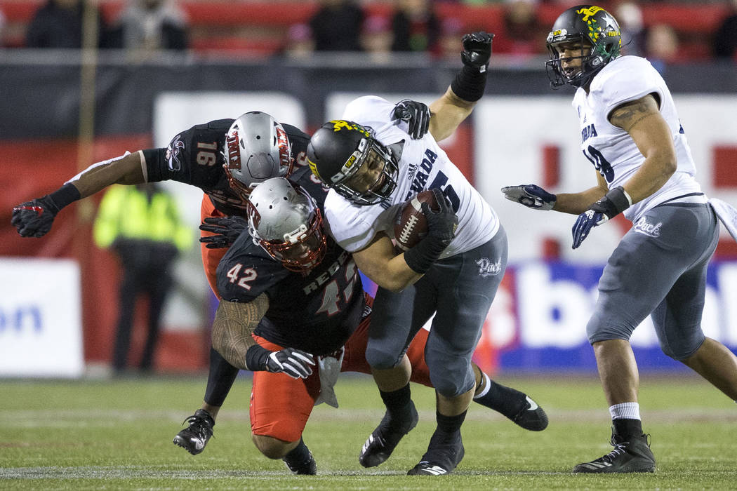 Nevada Wolf Pack running back Toa Taua (35), center, is tackled by UNLV Rebels defensive lineman Salanoa-Alo Wily (42) during the second half of an NCAA football game at Sam Boyd Stadium in Las Ve ...