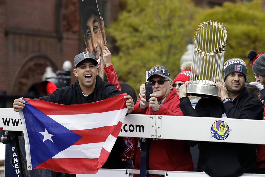 Boston Red Sox manager Alex Cora, left, waves the flag of Puerto Rico as coach Ramon Vazquez holds the championship trophy during a parade to celebrate the team's World Series championship over th ...