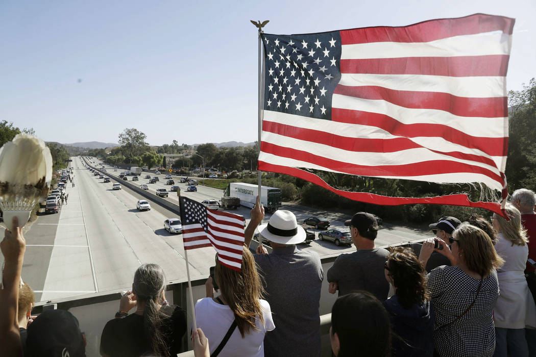 People look on from an overpass as a motorcade with the body of Ventura County Sheriff's Sgt. Ron Helus passes by Thursday, Nov. 8, 2018, in Newbury Park, Calif. Helus was fatally shot while respo ...