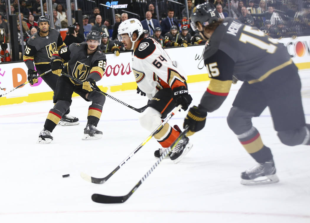 Golden Knights defenseman Nick Holden (22) passes the puck to Golden Knights defenseman Jon Merrill (15) in front of Anaheim Ducks right wing Kiefer Sherwood (64) during the first period of an NHL ...
