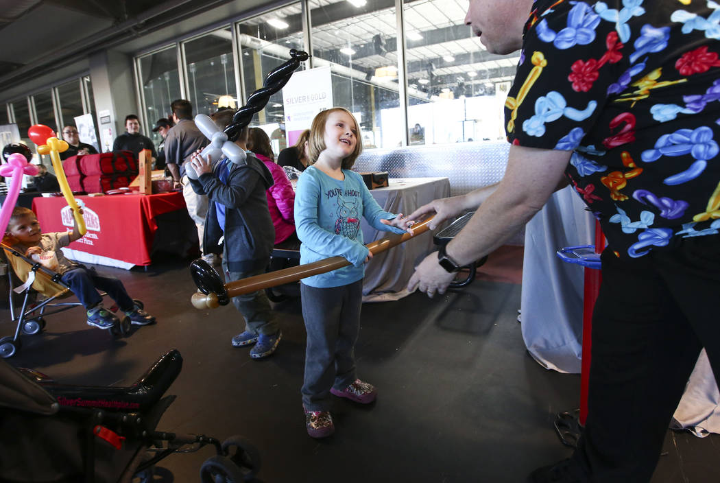 Balloon artist Roger Goodin hands a hockey stick balloon to Zoey Tuttle, 4, of North Las Vegas during the second annual "Silver and Gold" food drive at City National Arena in Las Vegas on Thursday ...