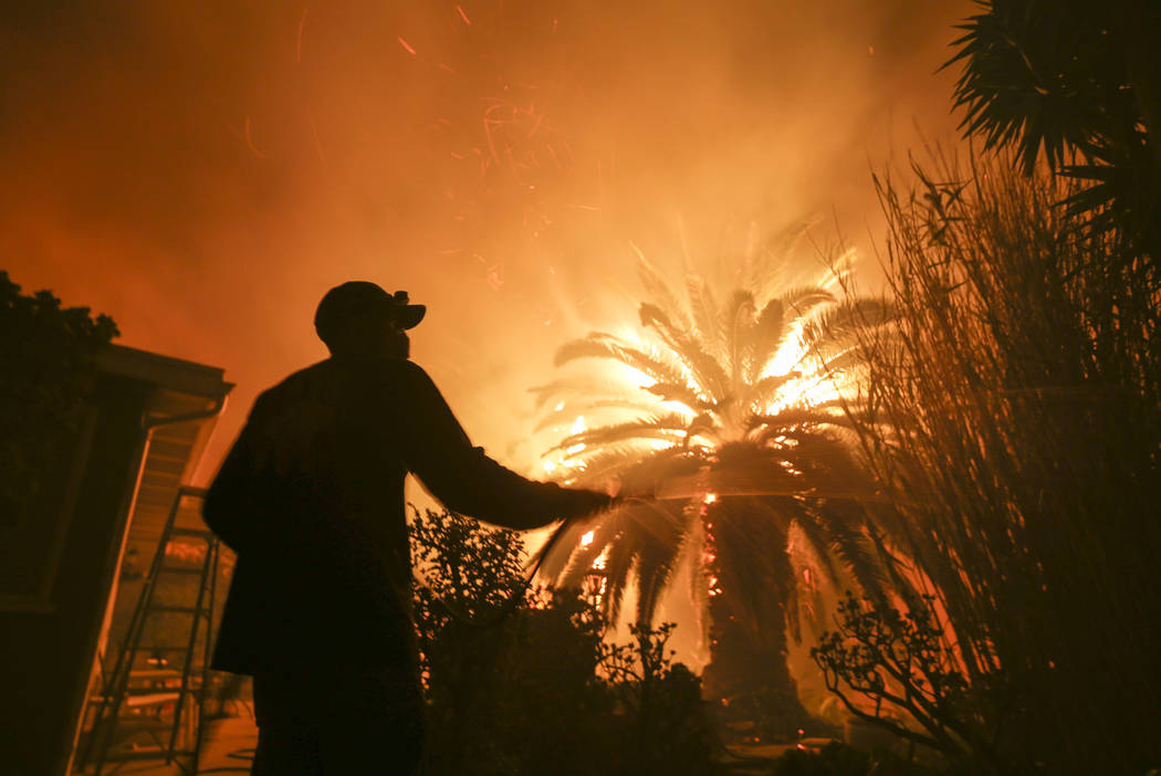 Park Billow, 27, sprays water on the hot spots in his backyard as the Woolsey Fire burns in Malibu, Calif., Friday, Nov. 9, 2018. (AP Photo/Ringo H.W. Chiu)