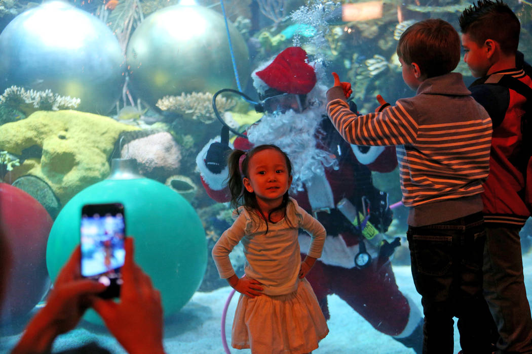 Alyssa Kim, 2, has her photo taken with Underwater Santa greets the crowd at Silverton hotel and casino in Las Vegas, Sunday, Dec. 2, 2018. He and the Christmas mermaid are in the aquarium every S ...