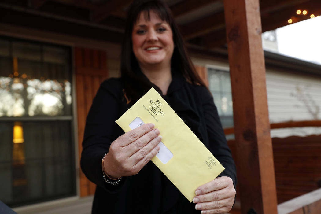 In this Dec. 20, 2018 photo, Reagen Adair holds on to an RIP Medical Debt yellow envelope as she poses for a photo at her home in Murchison, Texas. The co-founders of RIP Medical Debt buy millions ...