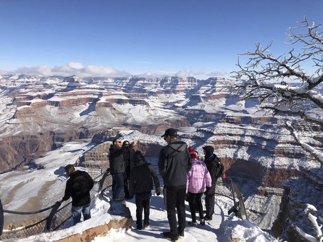 In this Tuesday, Jan. 1, 2019, photo, tourists look at and take photos of a snow-covered Grand Canyon, in Arizona. A winter storm has covered cactus with snow in parts of the American Southwest as ...