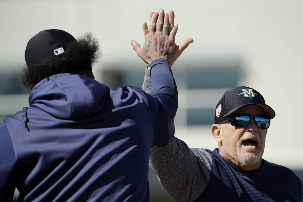 Seattle Mariners first base coach Perry Hill, right, high-fives pitcher Felix Hernandez during spring training baseball practice Saturday, Feb. 16, 2019, in Peoria, Ariz. (AP Photo/Charlie Riedel)