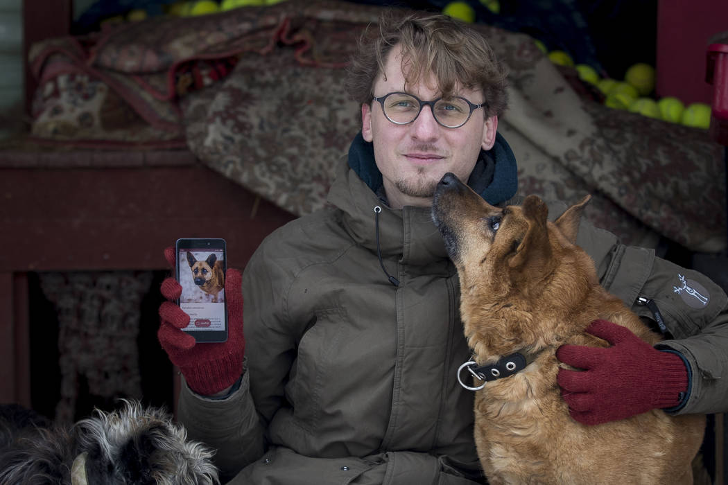 Vaidas Gecevicius, who developed an app helping to match stray dogs with potential owners, poses for a picture with a dog and shows this dog's profile on the app in Vilnius, Lithuania on Saturday, ...
