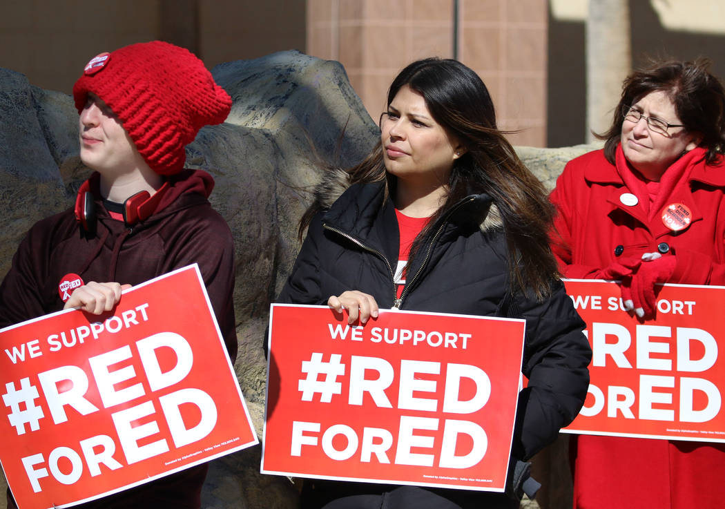 Alec Miller, left, Alicia Norman and Jana Pleggenkuhle, right, hold signs as they demonstrate their support for the ''Red for Ed'' movement outside of the Grant Sawyer Building on Monday, Feb. 18, ...