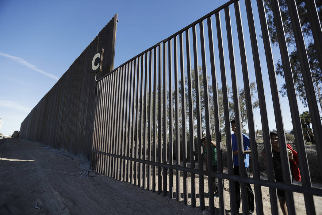 FILE - In this March 5, 2018, file photo, boys look through an older section of the border structure from Mexicali, Mexico, alongside a newly-constructed, taller section, left, in Calexico, Calif. ...