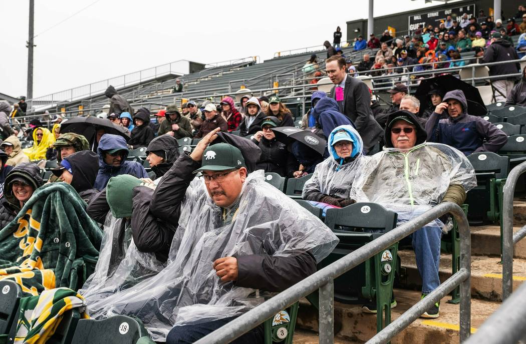 Fans at Hohokam Stadium try to cover up as rain settles in and ends up canceling a spring training baseball game between The Seattle Mariners and the Oakland Athletics after 1-1/2 innings Thursday ...