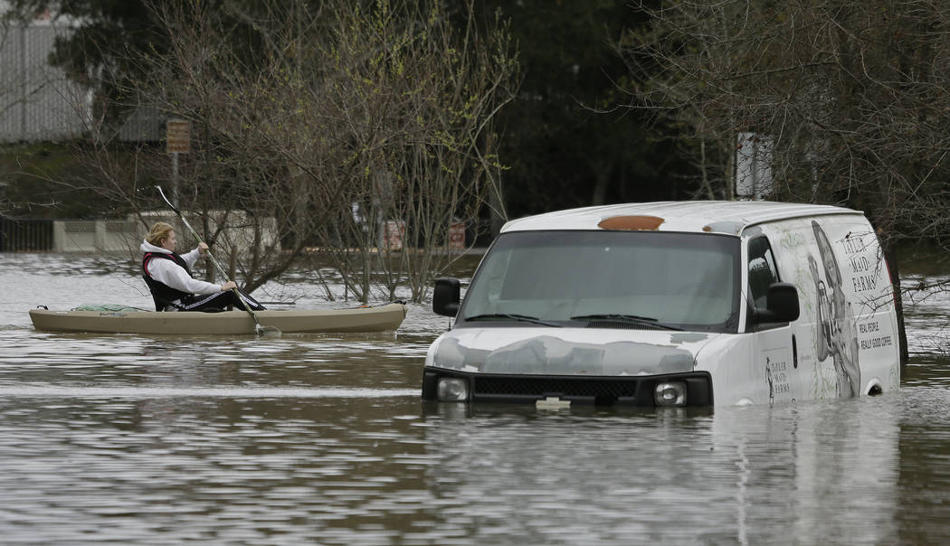 A man paddles past a submerged van in the flooded Barlow Market District parking lot Wednesday, Feb. 27, 2019, in Sebastopol, Calif. (Eric Risberg/AP)
