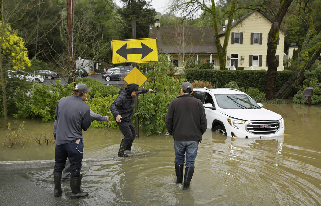 A group of men walk by a stranded car in flood water outside the Farmhouse Inn Wednesday, Feb. 27, 2019, in Forestville, Calif. (Eric Risberg/AP)