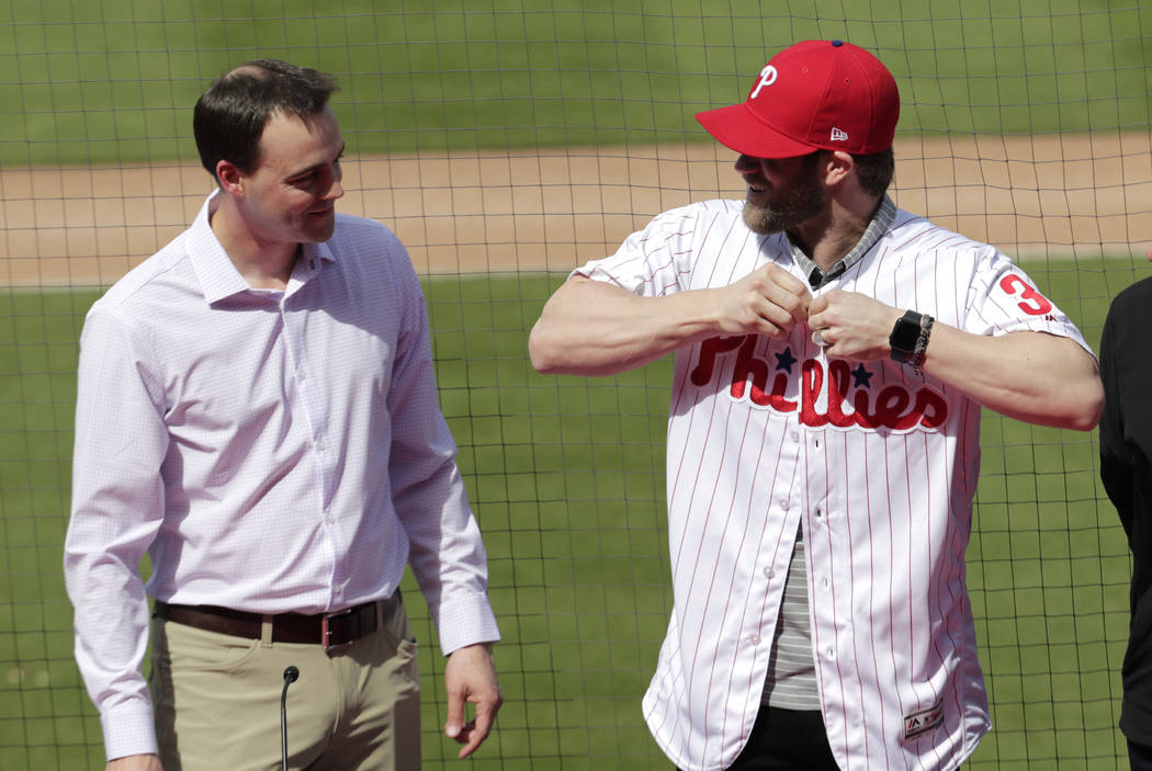 Philadelphia Phillies general manager Matthew Klentak, left, looks on as Bryce Harper puts on a Phillies jersey during a news conference at the team's spring training baseball facility, Saturday, ...