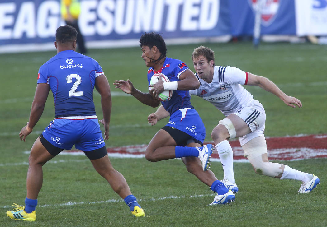 Samoa's John Valli, center, runs with the ball under pressure from USA's Ben Pinkelman while competing in the Cup Final during the USA Sevens Rugby Tournament at Sam Boyd Stadium in Las Vegas on S ...