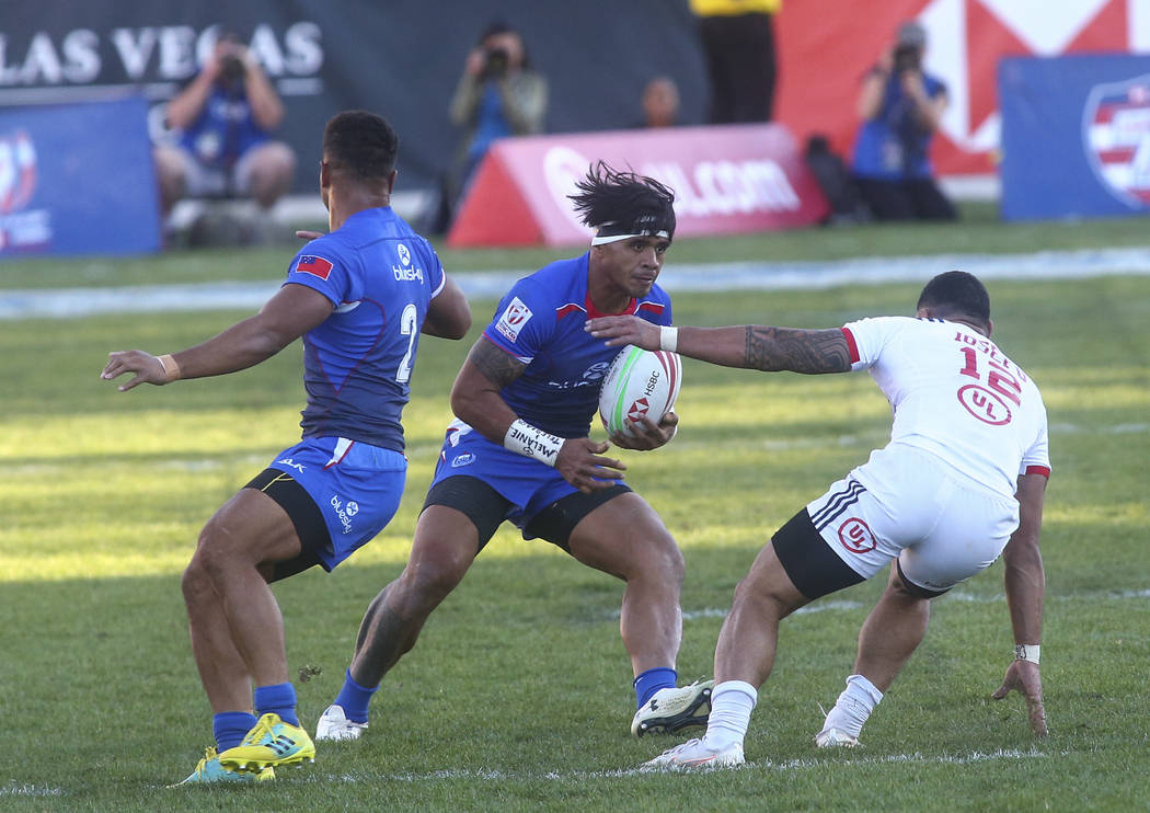 Samoa's Tofatu Solia, center, runs with the ball under pressure from USA's Martin Iosefo (12) while competing in the Cup Final during the USA Sevens Rugby Tournament at Sam Boyd Stadium in Las Veg ...