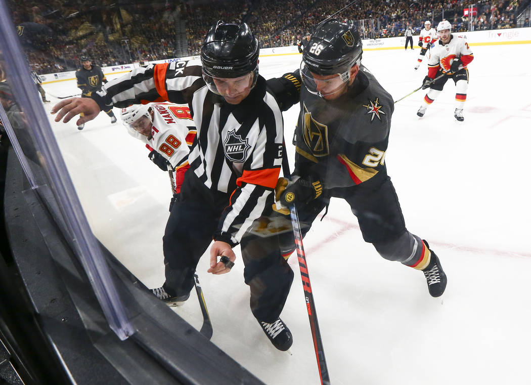 NHL referee Mike Hasenfratz tries to get out of the way of Golden Knights center Paul Stastny (26) and Calgary Flames left wing Andrew Mangiapane (88) as they battle for the puck during the second ...