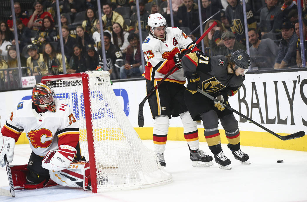 Golden Knights center William Karlsson (71) moves the puck under pressure from Calgary Flames center Sean Monahan (23) as goaltender David Rittich (33) looks on during the second period of an NHL ...