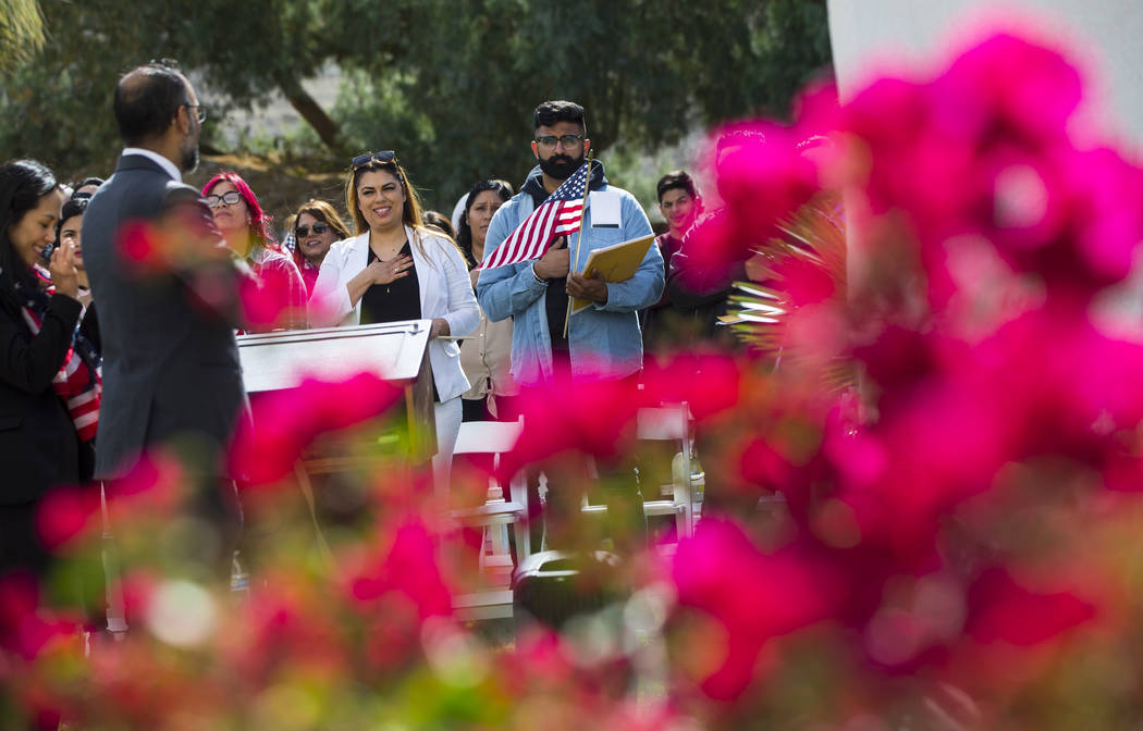 Irma Martinez of Tehachapi, Calif., who immigrated from Mexico, center left, and Mandeep Sidha, of Los Angeles, who immigrated from India, sing along to the national anthem during a naturalization ...