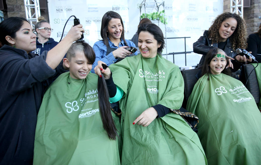 Katrin Ivanoff, of Las Vegas, center, with her children Ilian Ivanoff, 10, and daughter Katrin Ivanoff, 9, get their heads shaved by, from left, Genevie Valdivia, Kristina Rodriguez and Brianna Br ...