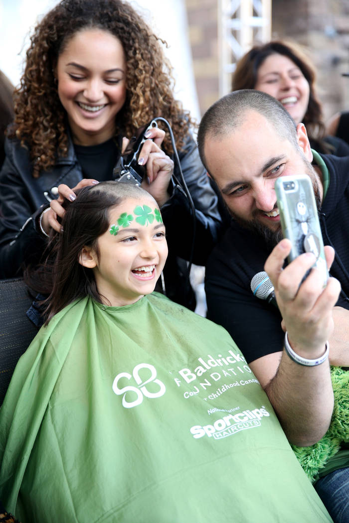 Katrin Ivanoff, 9, of Las Vegas, get her head shaved by Brianna Brown of Las Vegas, as Vegas Golden Knights host and radio personality Wayne 'Big D' Danielson shows her progress during St. Baldric ...
