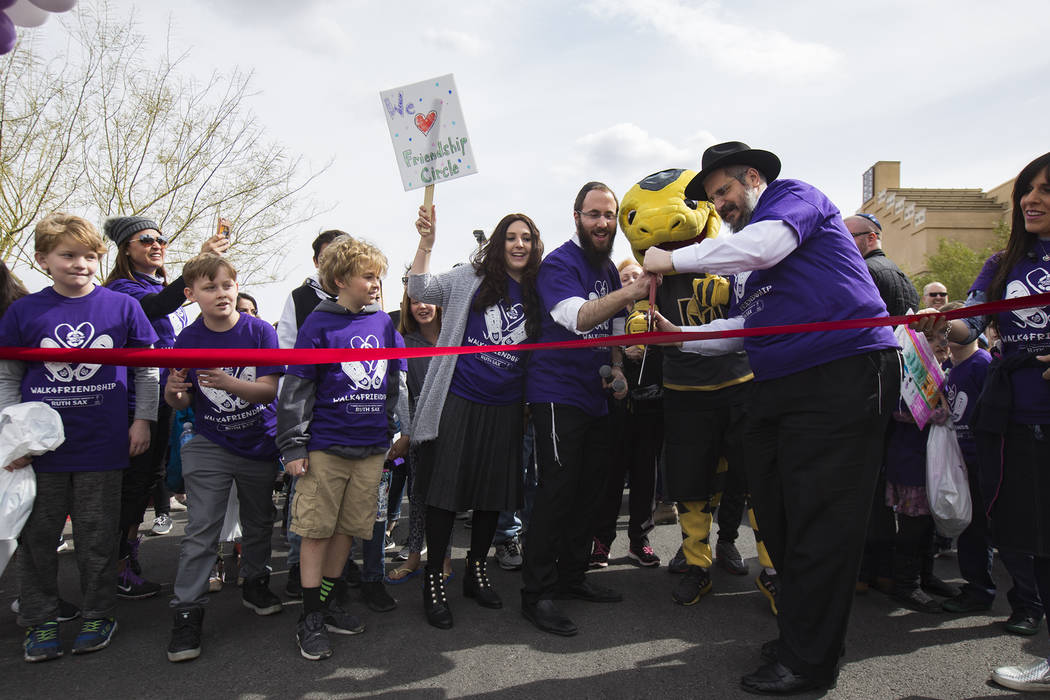 Nechama Harlig, holding a sign, from left, her husband Rabbi Levi Harlig, Chance the Golden Knights mascot, and Levi's father Rabbi Shea Harlig cut the ribbon to begin a walk from Bet Yossef Comm ...