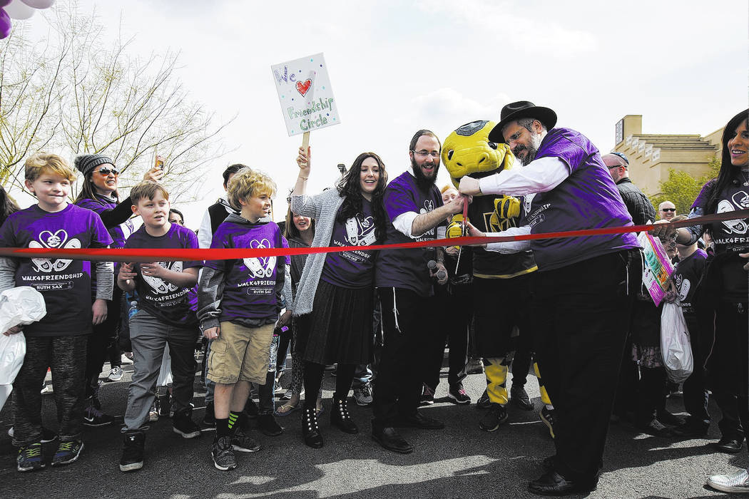 Nechama Harlig, holding a sign, from left, her husband Rabbi Levi Harlig, Chance the Golden Knights mascot, and Levi's father Rabbi Shea Harlig cut the ribbon to begin a walk from Bet Yossef Comm ...