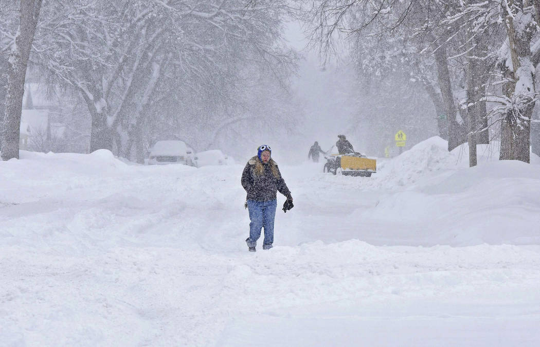 Diane Halverson walks through falling snow on Fifth Street in Bismarck, N.D., on Saturday morning, March 9, 2019, as snow removal crews begin clearing sidewalks and parking lots near the downtown ...