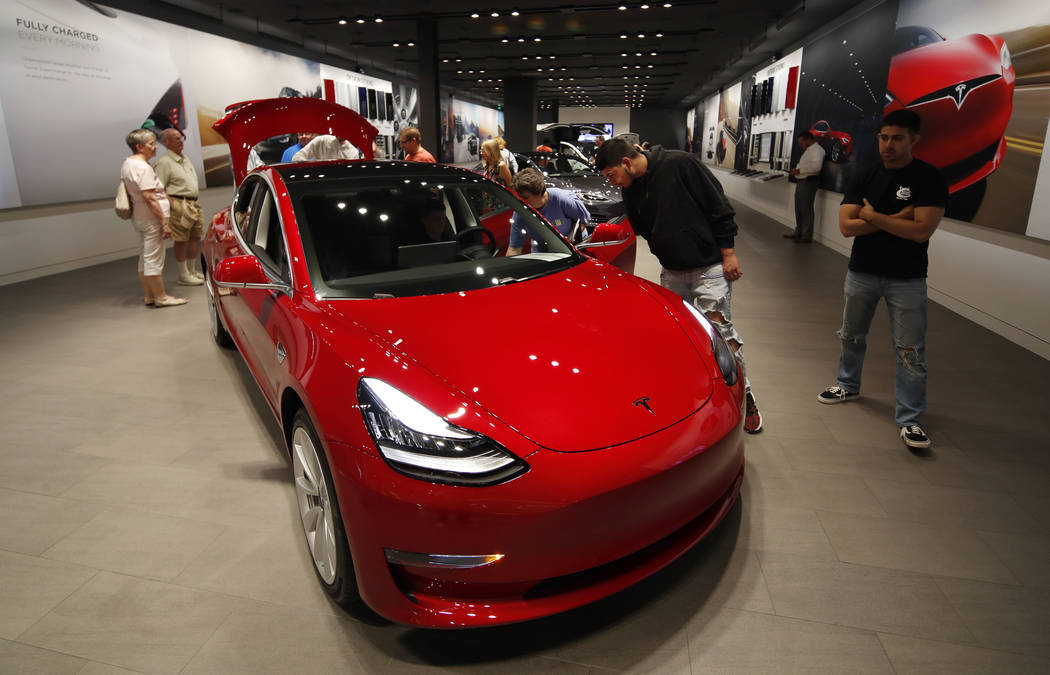 Prospective customers confer with sales associates as a Model 3 sits on display in a Tesla showroom in the Cherry Creek Mall in Denver. (AP Photo/David Zalubowski, File)