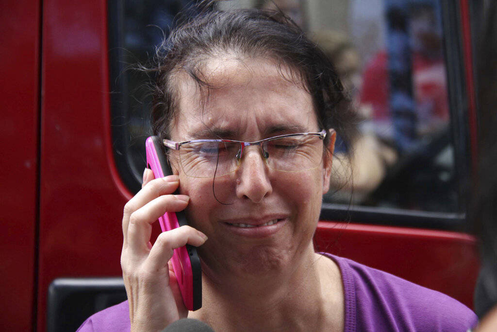 A woman uses her cell phone as she waits for news outside the Raul Brasil State School in Suzano, Sao Paulo state, Brazil, Wednesday, March 13, 2019. The state government of Sao Paulo said two tee ...