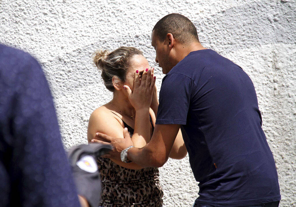 A man comforts a woman at the Raul Brasil State School in Suzano, Brazil, Wednesday, March 13, 2019. The state government of Sao Paulo said two teenagers, armed with guns and wearing hoods, entere ...