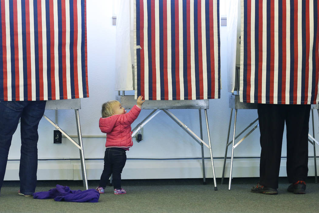 Zoe Buck, a 14-month-old child, checks out an empty voting booth as at her mother, Julie Buck, votes at left, Tuesday Nov. 4, 2014, at the Alaska Zoo polling place in Anchorage, Alaska. (Ted S. Wa ...
