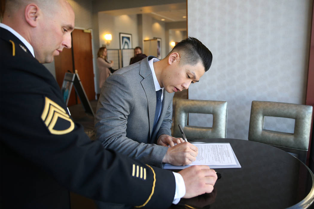 Anthony Hua, right, with U.S. Army Staff Sgt. Zachary Anderson, a health care recruiter, signs his contract after getting sworn in as U.S. Army Reserve captain during a ceremony at the Hampton In ...