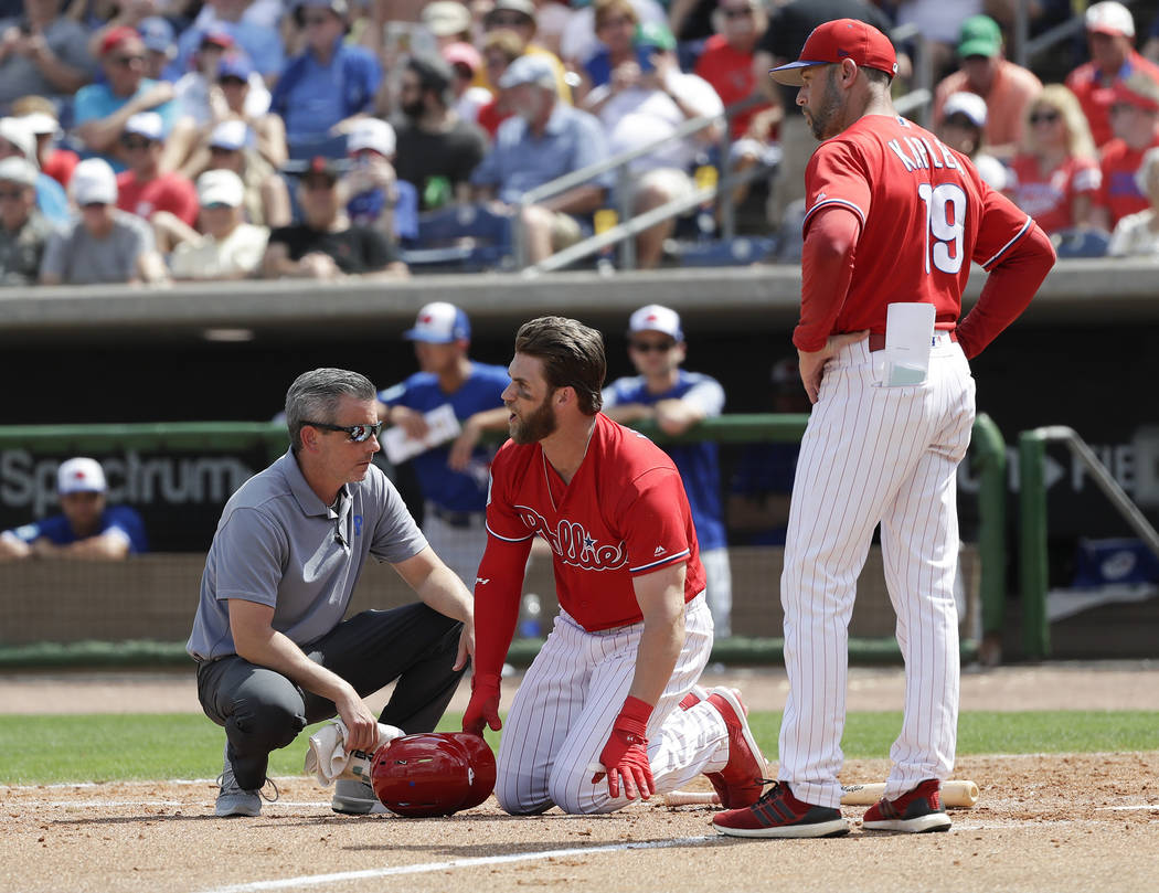Philadelphia Phillies' Bryce Harper, center, yells toward Toronto Blue Jays pitcher Trent Thornton as manager Gabe Kapler, right, and assistant trainer Chris Mudd check on him after he was hit by ...