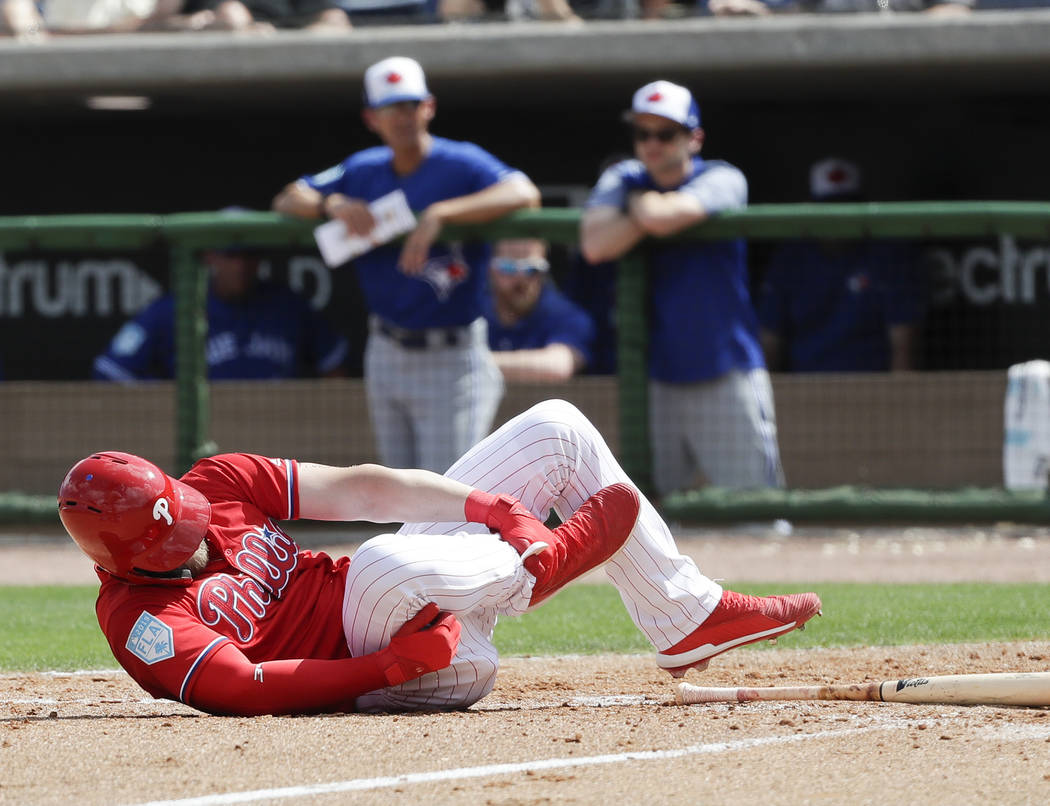 Philadelphia Phillies' Bryce Harper rolls on the dirt holding his leg after getting hit by a pitch against the Toronto Blue Jays during the sixth inning in a spring training baseball game, Friday, ...