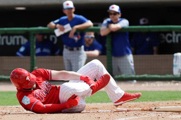 Philadelphia Phillies' Bryce Harper rolls on the dirt holding his leg after getting hit by a pitch against the Toronto Blue Jays during the sixth inning in a spring training baseball game, Friday, ...