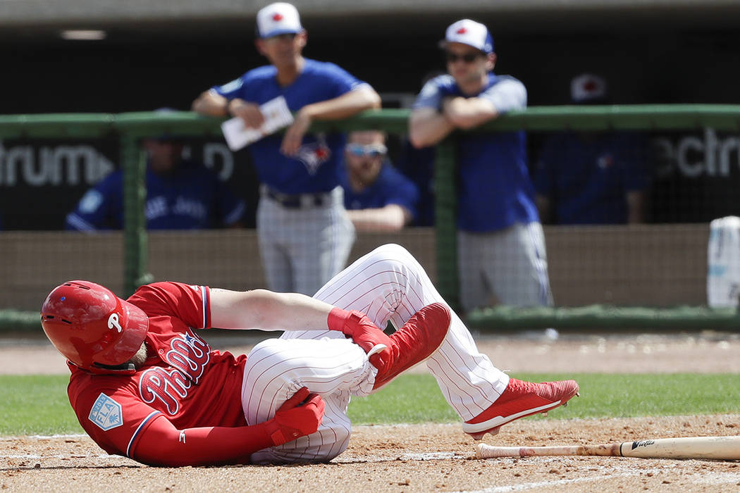 Philadelphia Phillies' Bryce Harper rolls on the dirt holding his leg after getting hit by a pitch against the Toronto Blue Jays during the sixth inning in a spring training baseball game, Friday, ...