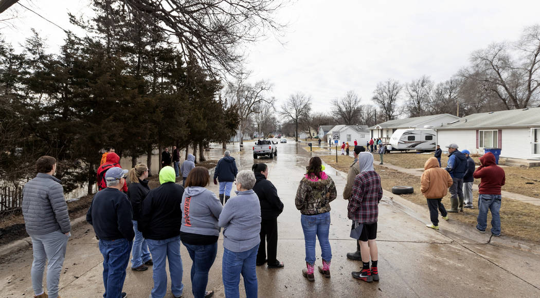 A crowd gathers to watch residents make their way in and out of a flooded neighborhood Sunday, March 17, 2019, in Omaha, Neb. Hundreds of people were evacuated from their homes in Nebraska and Io ...