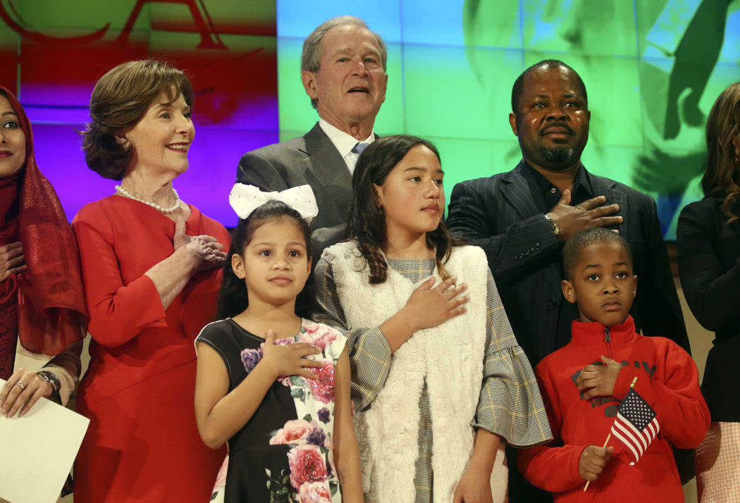 Former President George W. Bush and former first lady Laura Bush recite the pledge of allegiance with new U.S. citizens, including Felix Odeh, (top right) of Nigeria, during a naturalization cerem ...