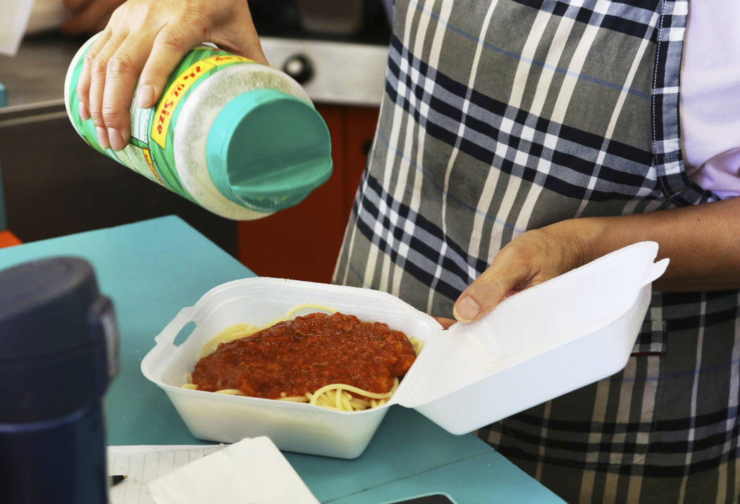 In this Thursday, March 14, 2019 photo, Belinda Lau, manager of the Wiki Wiki Drive Inn takeout restaurant in Honolulu, sprinkles cheese on an order of spaghetti in a styrofoam container. Hawaii w ...
