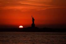 In this July 1, 2018 file photo, the sun sets behind the Statue of Liberty in New York as record high temperatures were recorded over the week in the U.S. and elsewhere. An AP data analysis of rec ...