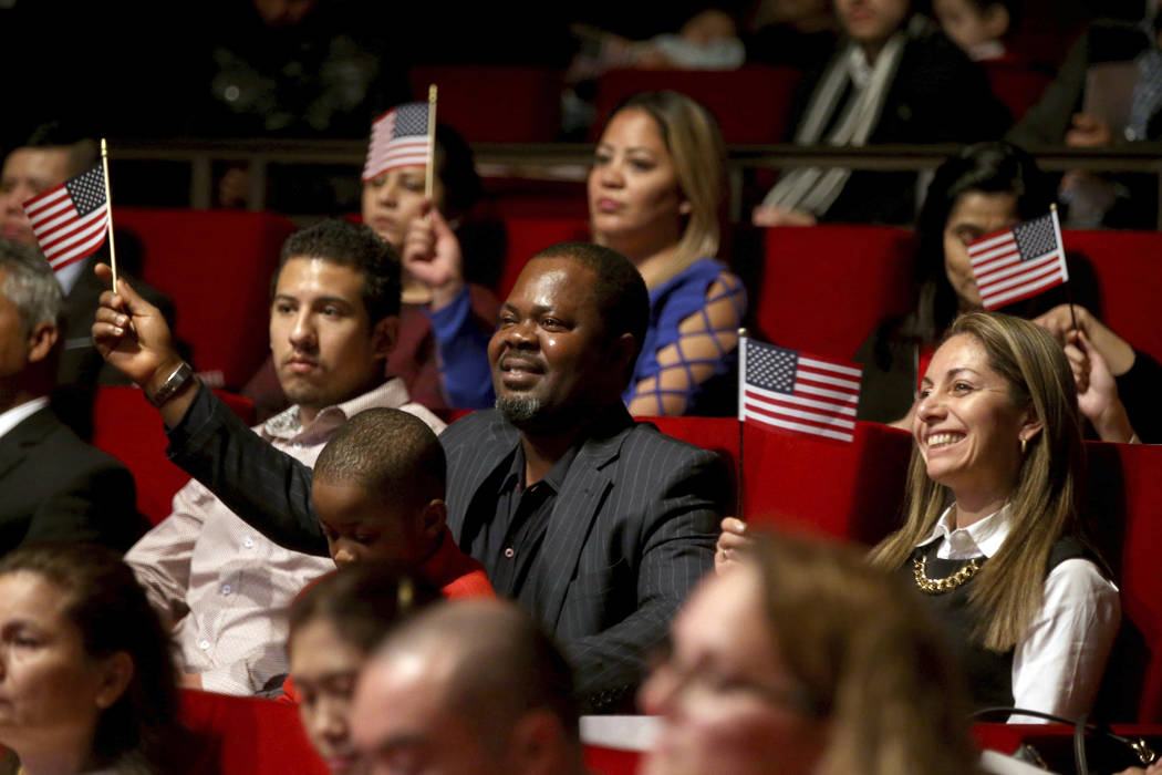 New U.S. citizen Felix Odeh, of Nigeria, (center) and other new citizens wave American flags as "God Bless America" is sung during a naturalization ceremony at the George W. Bush Preside ...