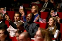 New U.S. citizen Felix Odeh, of Nigeria, (center) and other new citizens wave American flags as "God Bless America" is sung during a naturalization ceremony at the George W. Bush Preside ...