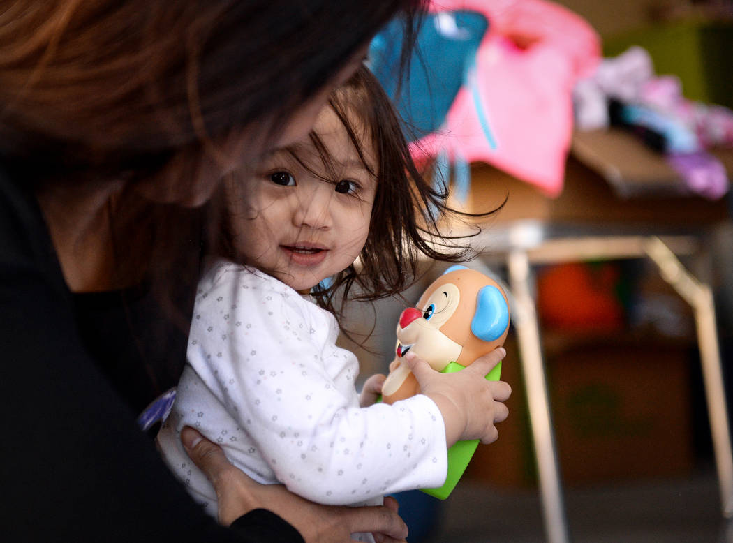 Ava Cruz, 1, holds an item she found at a yard sale while being held by her mother, Aura Carreo ...