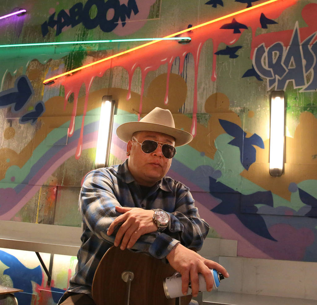 Tiki Jay One, an Urban Landscapist/Commercial Designer, poses for a photo in front of the mural ...