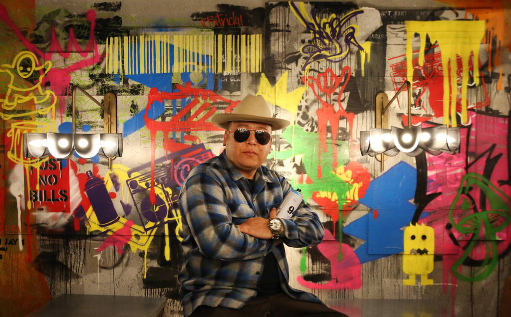 Tiki Jay One, an Urban Landscapist/Commercial Designer, poses for a photo in front of the mural ...