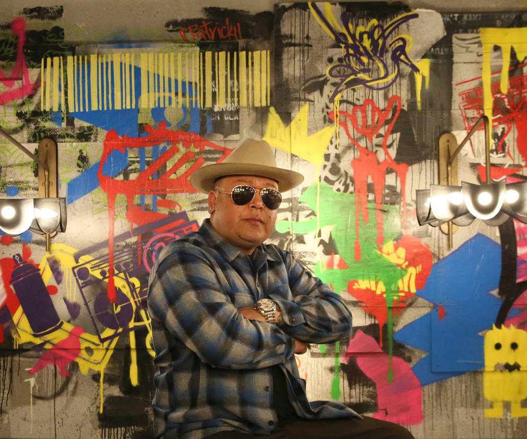 Tiki Jay One, an Urban Landscapist/Commercial Designer, poses for a photo in front of the mural ...