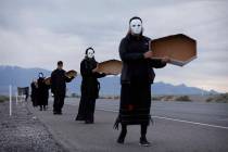 People wear masks and hold signs in the shape of coffins during a protest against drone warfare ...